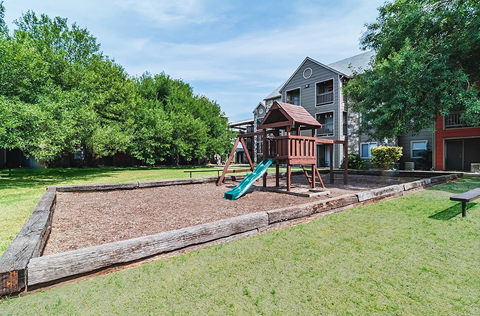 A playground area with a slide and a wooden structure is in front of a two-story house.