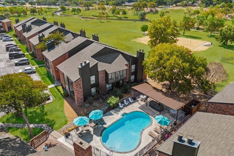 A swimming pool is surrounded by a patio with chairs and umbrellas.