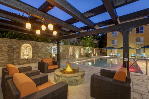 Apartments in Burbank, CA  Pergola with Fire Pit and Seating Area View of Pool with Lounge Chairs Lit Up at Night.jpg