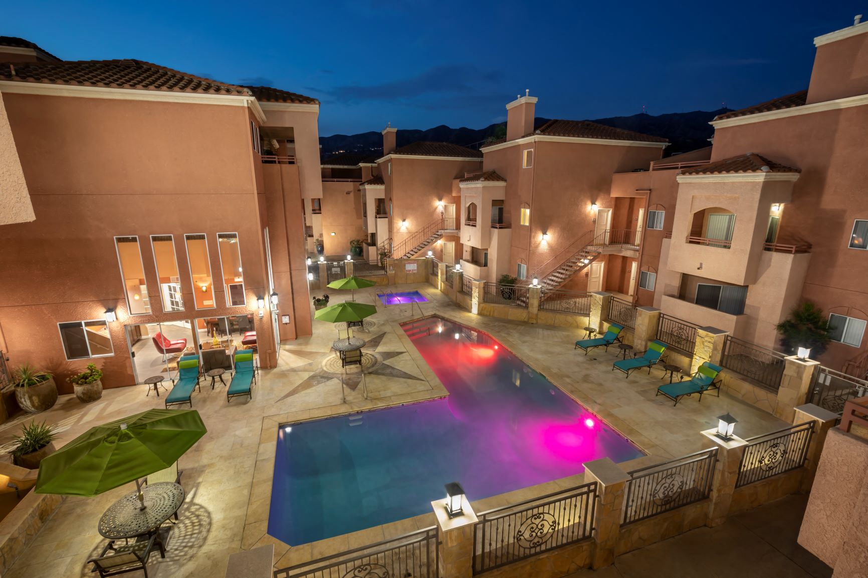 Apartments in Burbank, CA -  Aerial View of Lit Up Pool and Patio, Jacuzzi,  Tables and Surrounding Buildings