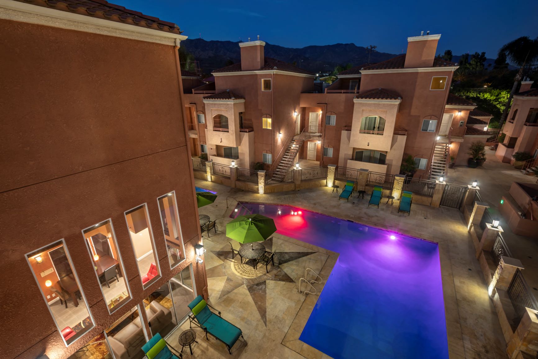 Apartments in Burbank, CA - Aerial View of Lit Up Pool and Patio with Lounge Chairs and Tables and Surrounding Buildings scott villa