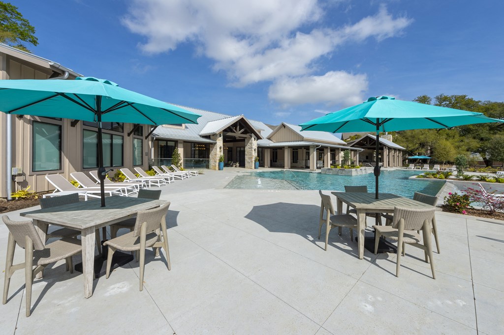 a patio with tables and umbrellas next to a swimming pool