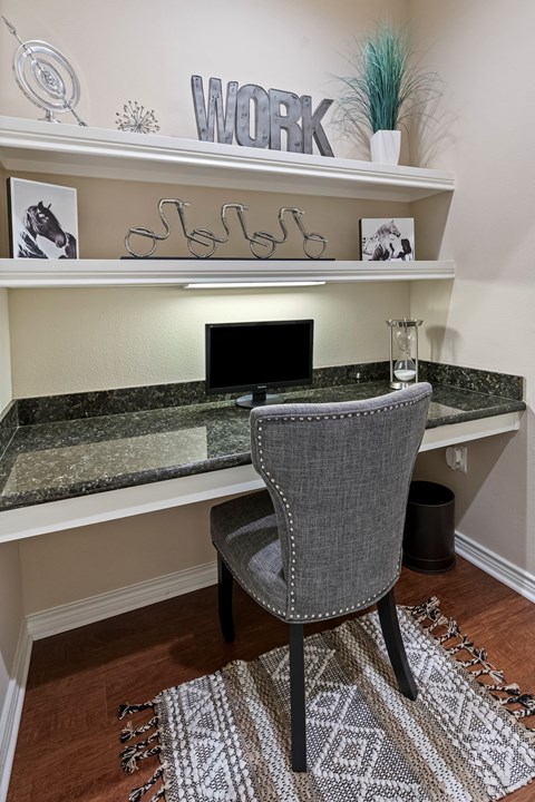 A grey chair is in front of a desk with a computer on it.