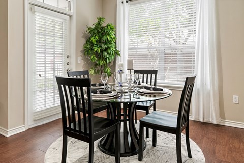 A dining room with a table set for two and a potted plant.
