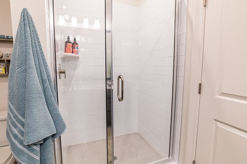 a shower with a glass door and a blue towel in a bathroom