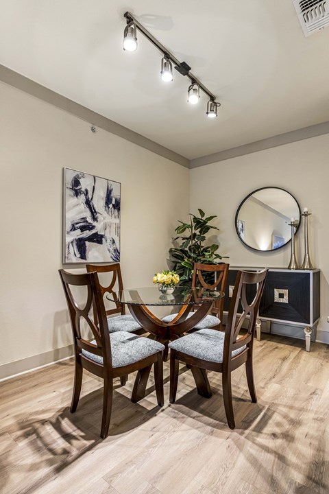 A dining room with a round mirror and a vase of flowers on the table.