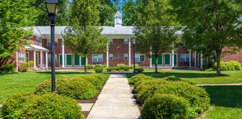 a brick building with green shutters and a lawn and trees in front of it at Nottingham Manor Apartments, Montvale, NJ, 07645