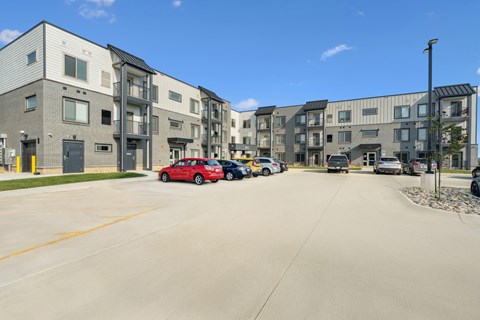 A red car is parked in a parking lot in front of a building.