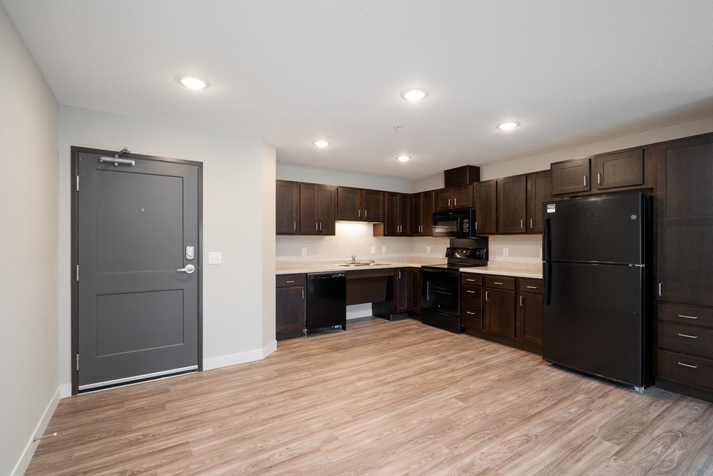 a kitchen with black appliances and wooden flooring and dark cabinets