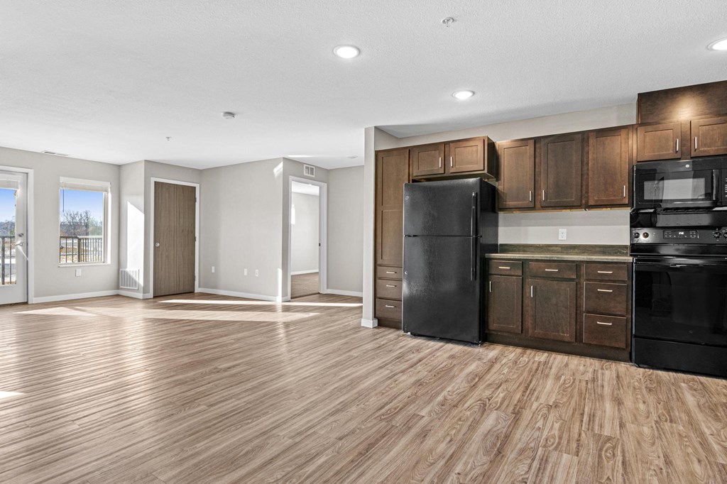 an empty kitchen with black appliances and wooden floors