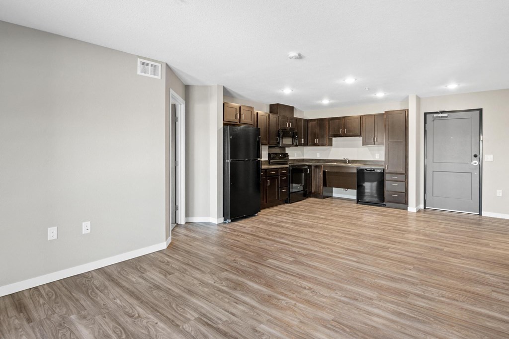 an empty living room with a kitchen with a refrigerator and