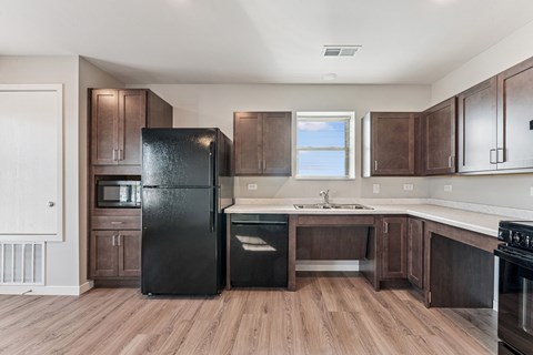 A black fridge stands in a kitchen with wooden floors and brown cabinets.