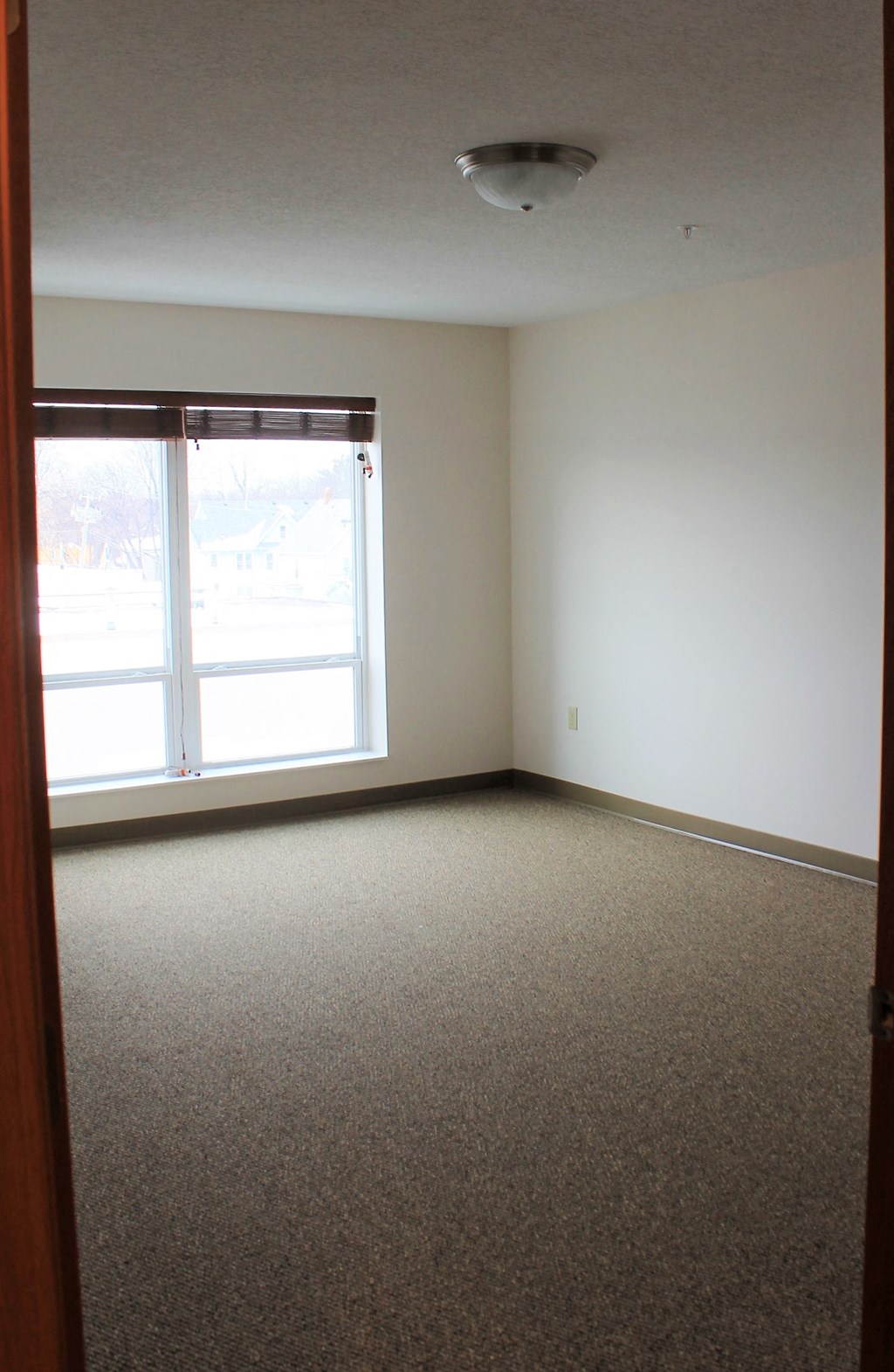 A room with a carpeted floor and a window with blinds.