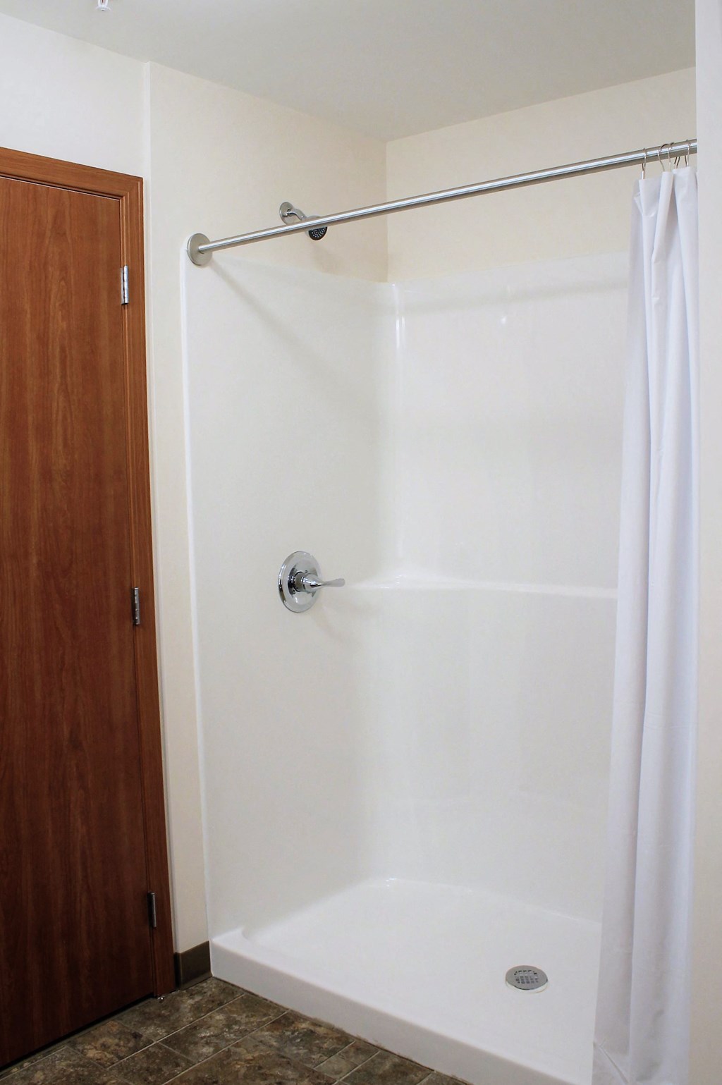 A white shower stall with a white shower curtain and a silver shower head.
