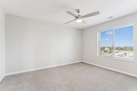 A room with a ceiling fan and a window overlooking a parking lot.
