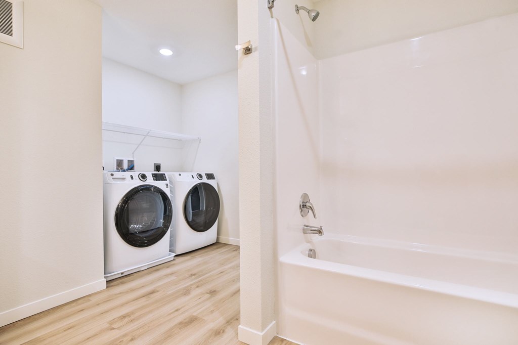 A white bathroom with a tub and two washing machines.