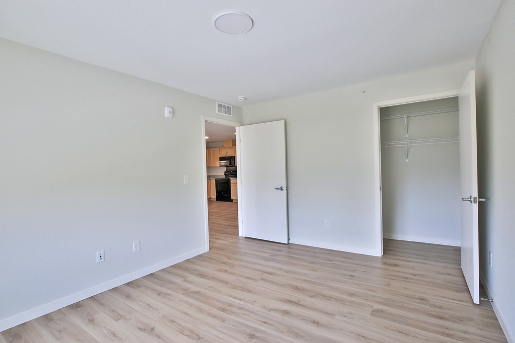 A room with white walls and wooden flooring, with two doors and one open to a kitchen.