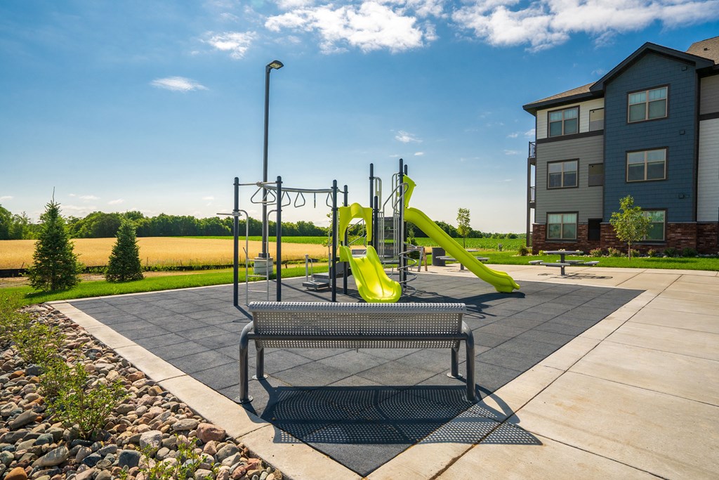 a playground with a yellow slide and a picnic table in front of an apartment building