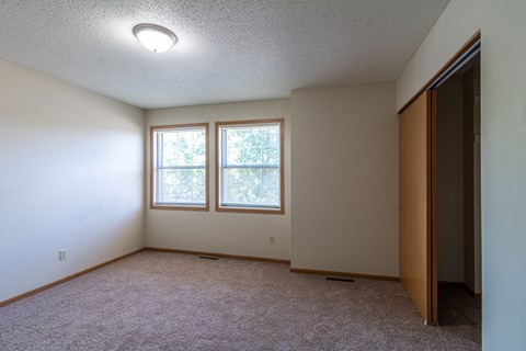 A room with a carpeted floor, a window with trees visible outside, and a closed door on the right.