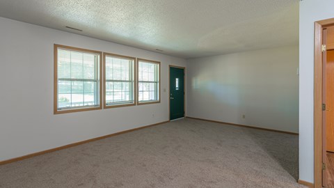 A room with a carpeted floor, a door, and a window with blinds.