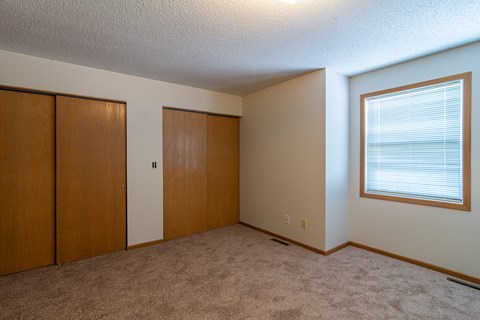 A room with a carpeted floor and a window with blinds.
