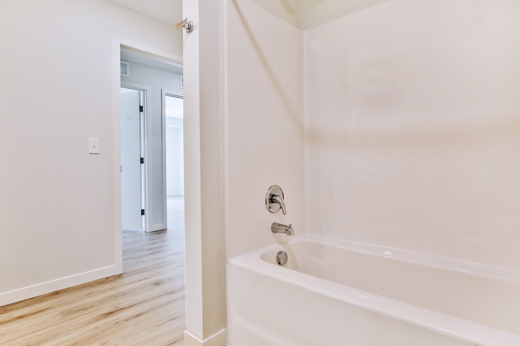 A white bathroom with a tub and a doorway to another room.