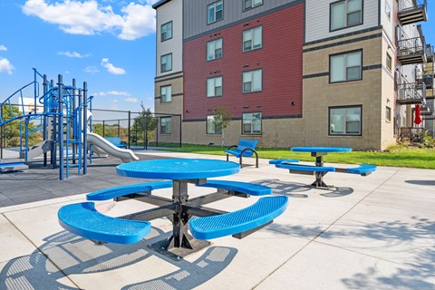 a playground and picnic area at an apartment building with blue tables and chairs