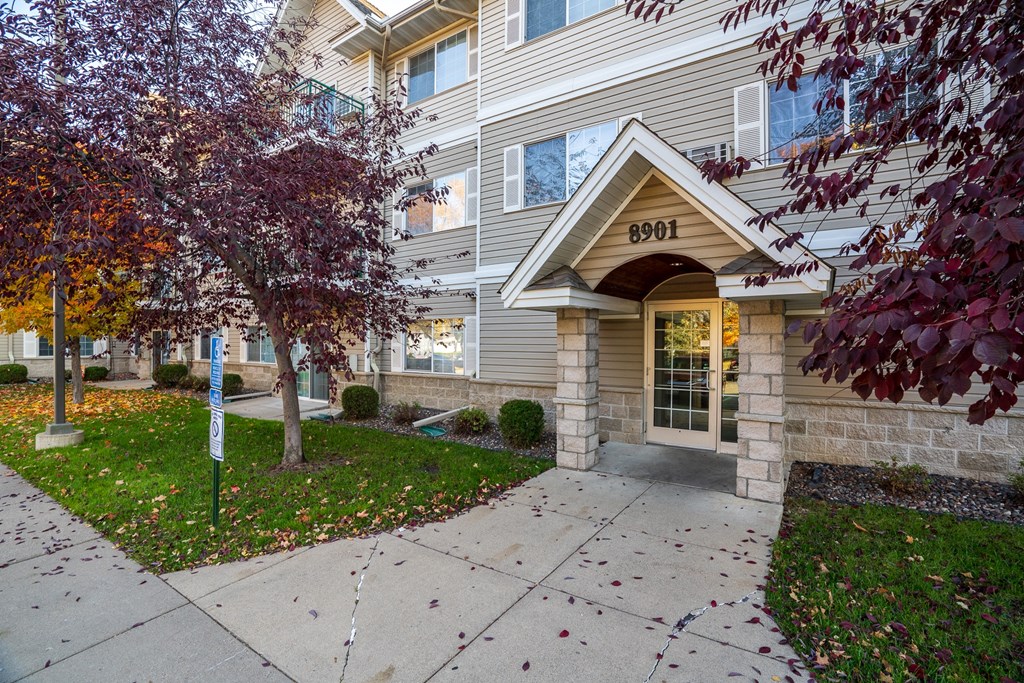 the walkway to the front of a building with a sidewalk and tree