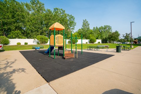 A playground with a yellow and green structure in the middle of a paved area.