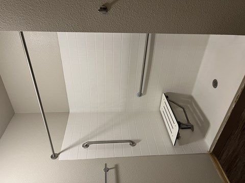 A white tiled shower with a metal rod and a white shower caddy.
