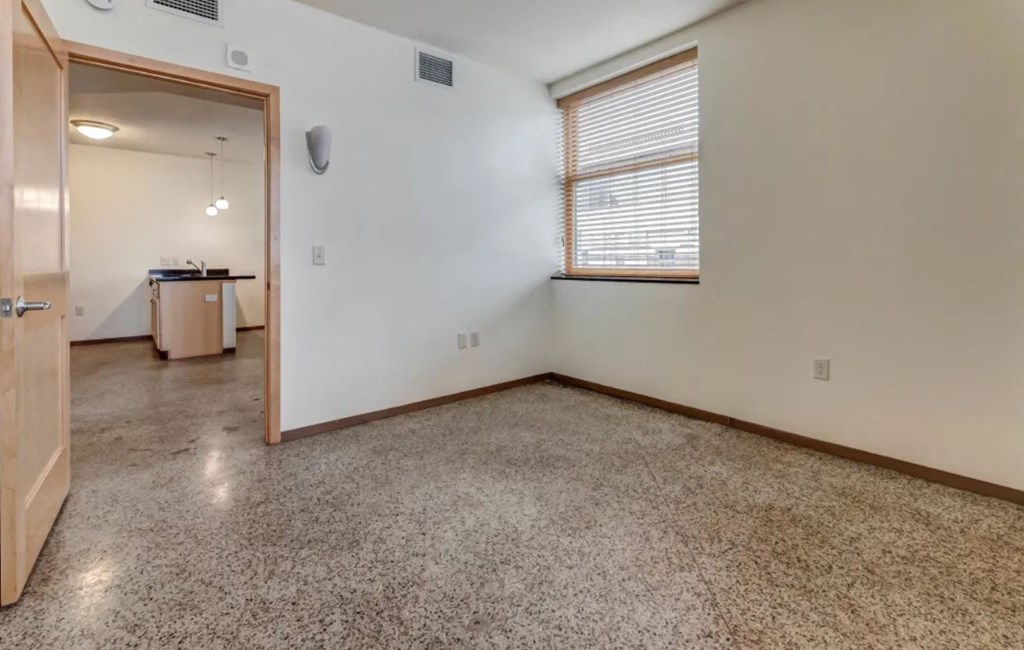 an empty living room with a window and a door to a kitchen