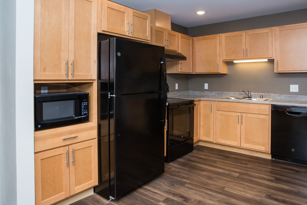 A black refrigerator stands in a kitchen with wooden cabinets.