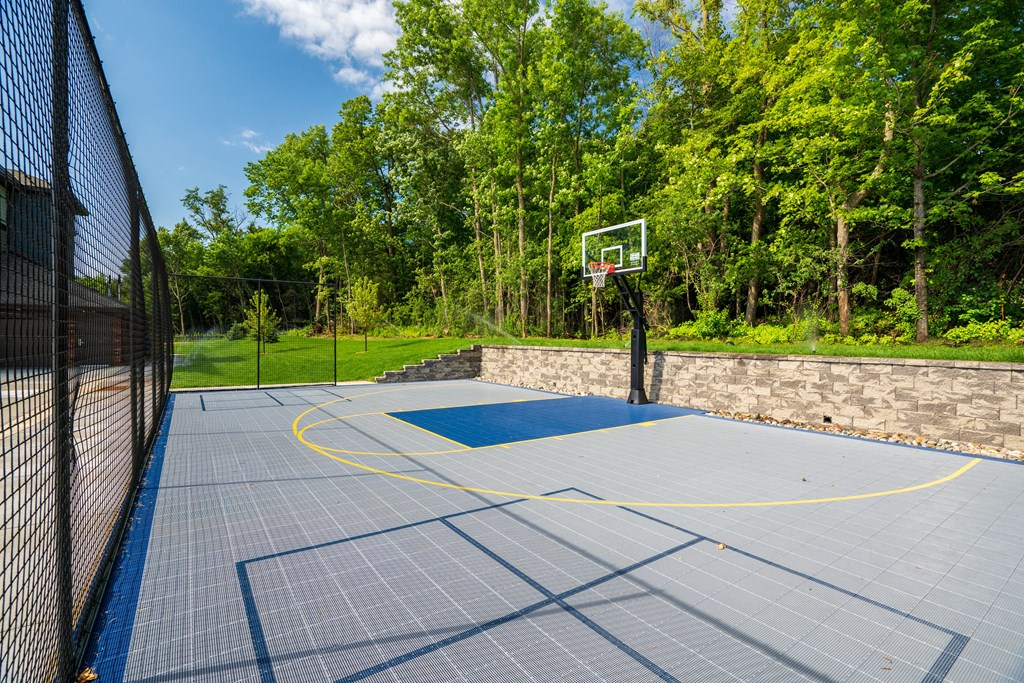 the basketball court is located on a concrete surface with a fence and trees