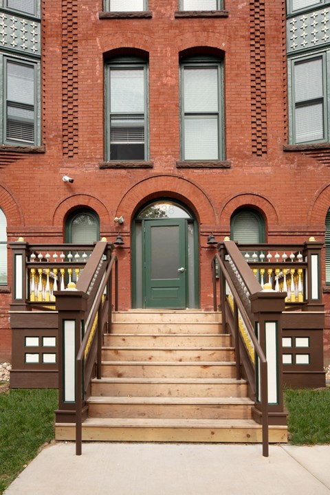A red brick building with a green door and a wooden staircase.