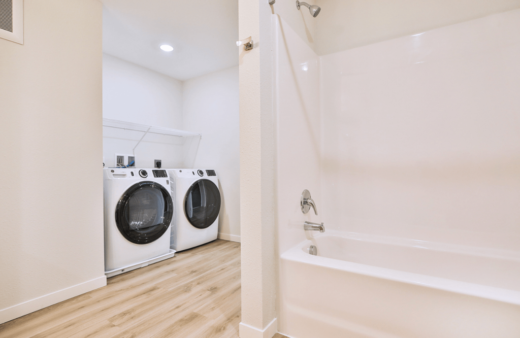 A white bathroom with a tub and two washing machines.
