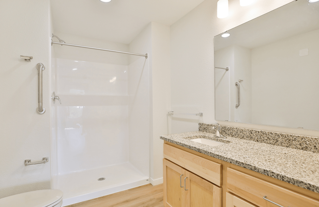 A white bathroom with a walk-in shower and a marble countertop.