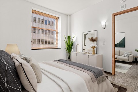 A bedroom with a bed, a mirror, and a window with blinds.