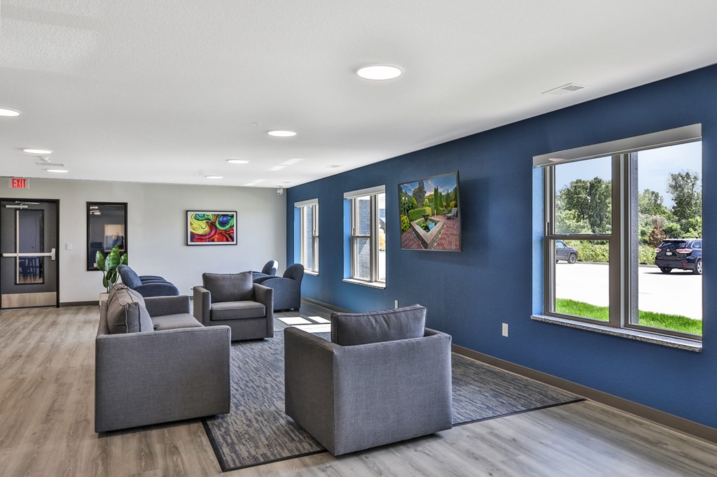 A spacious waiting room with grey couches and a view of the street outside.