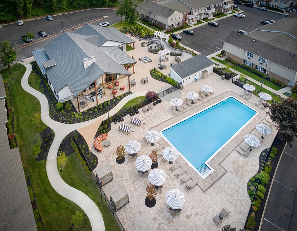 an aerial view of a swimming pool and patio with umbrellas and the clubhouse at Heritage Oyster Bay, East Norwich, NY