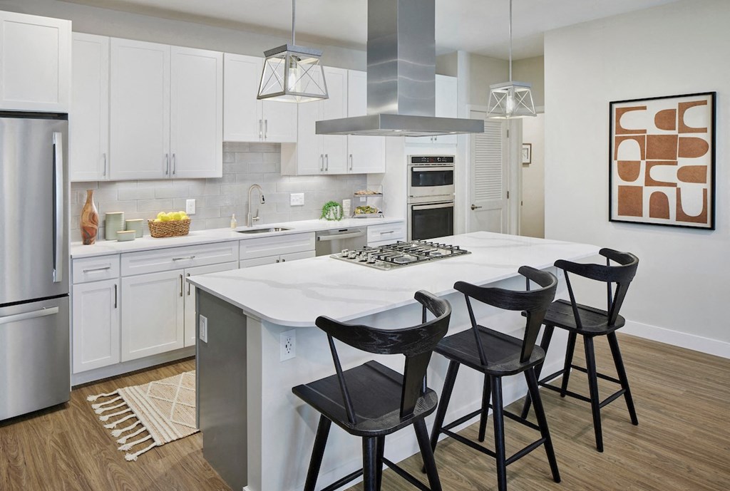 a kitchen with white cabinets and a large white island with three black stools