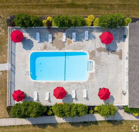 An aerial view of a pool surrounded by red umbrellas and trees.