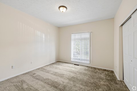 A room with a carpeted floor and a window with blinds.