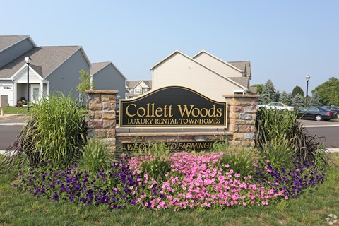 A sign for Collett Woods Luxury Rental Townhomes is surrounded by flowers.