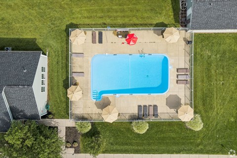 A large swimming pool surrounded by a concrete patio and a small white house.