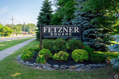 A sign that says Fetzner Square is in front of a green bush.