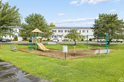 A playground with a slide and a sign in the middle of the grass.