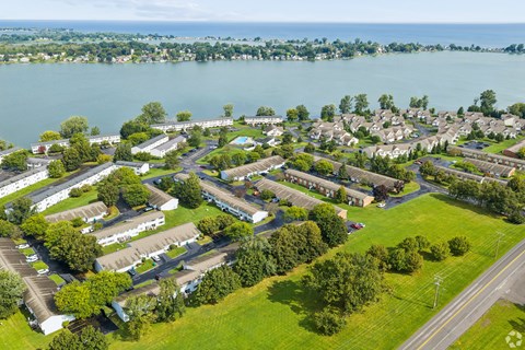 A bird's eye view of a residential area with houses, trees, and a body of water in the background.