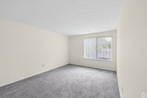 A room with a carpeted floor and a window with blinds.