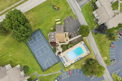 A tennis court is surrounded by a parking lot and a pool.