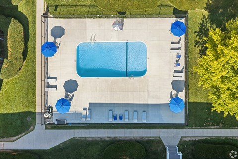 An aerial view of a pool surrounded by a concrete deck and blue umbrellas.